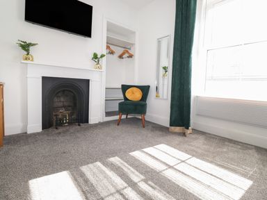 A room with a fireplace a green chair with a yellow cushion a wall mirror and a window at Aryelle House in Kendal