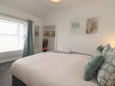 A bedroom with a large bed with folded towels and pillows next to a window with curtains at Aryelle House in Kendal