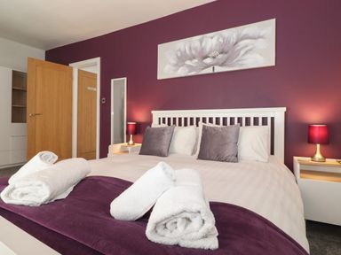 A bedroom with a white bed frame purple pillows and lamps on white bedside tables at Aryelle House in Kendal
