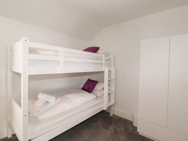 A bedroom with a white bunk bed with purple pillows and a white wardrobe at Aryelle House in Kendal
