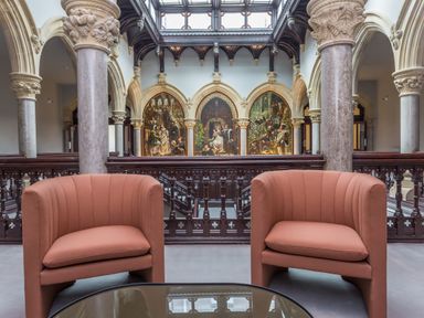A seating area with two orange armchairs and a glass table in front of arches and paintings at The Mabel Suite Stone Cross Mansion in Ulverston