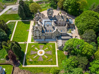 A large stone mansion with symmetrical gardens and paved pathways surrounded by trees at The Mabel Suite Stone Cross Mansion in Ulverston
