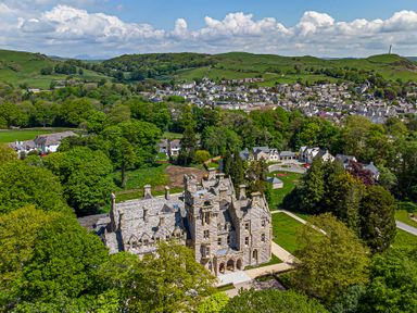 An aerial view of a large stone mansion surrounded by trees with a village and green hills in the background at The Mabel Suite Stone Cross Mansion in Ulverston