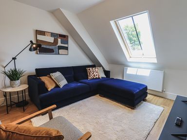A living room with a dark blue sectional sofa pillows a lamp a plant an armchair and a skylight window at The Mabel Suite Stone Cross Mansion in Ulverston