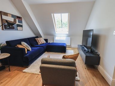 A living room with a blue sectional sofa a TV on a black stand and a skylight at The Mabel Suite Stone Cross Mansion in Ulverston