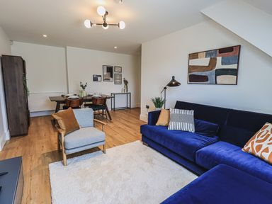 A living room with a blue sofa armchair dining table and wall art at The Mabel Suite Stone Cross Mansion in Ulverston