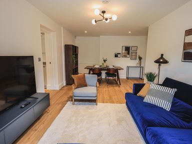 A living room with a blue sofa and gray armchair a dining table with four chairs and a TV on a stand at The Mabel Suite Stone Cross Mansion in Ulverston