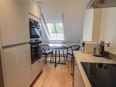 A kitchen with built in oven, glass dining table with chairs, kettle and coffee machine on counter at The Mabel Suite Stone Cross Mansion in Ulverston