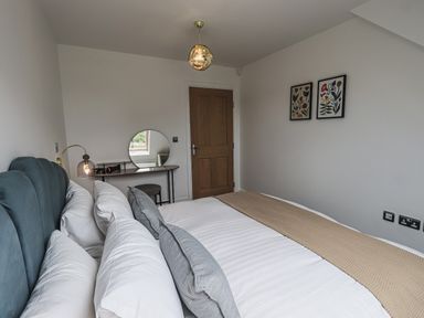 A bedroom with a bed multiple pillows a dressing table round mirror and two framed pictures on the wall at The Mabel Suite Stone Cross Mansion Ulverston