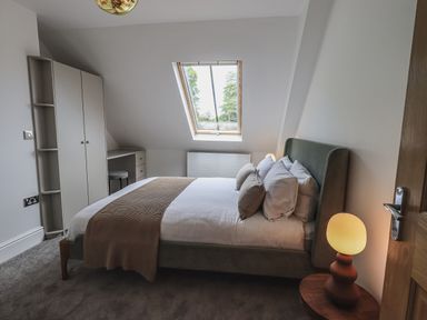 A bedroom with a bed pillows a bedside lamp a wardrobe and a skylight window at The Mabel Suite Stone Cross Mansion in Ulverston