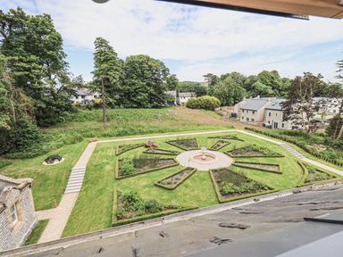 A garden with a circular flower bed and a central fountain surrounded by paths and grass at The Mabel Suite Stone Cross Mansion in Ulverston