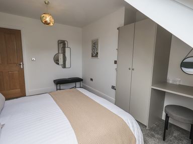 A bedroom with a bed, wardrobe, bench, desk with stool, and mirrors on the wall at The Mabel Suite Stone Cross Mansion Ulverston