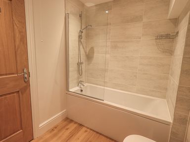 A bathroom with a wooden door a bathtub with a showerhead and a glass screen at The Mabel Suite Stone Cross Mansion in Ulverston