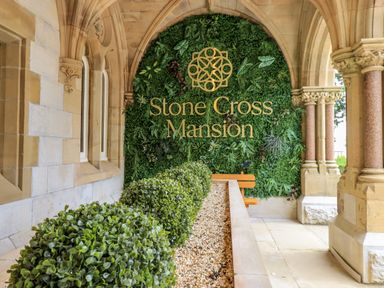A stone archway with columns and trimmed bushes in front of a green wall with Stone Cross Mansion text at The Mabel Suite Stone Cross Mansion in Ulverston