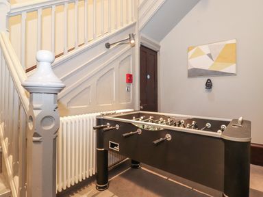 A foosball table under a staircase with a radiator and a geometric wall painting at The Mabel Suite Stone Cross Mansion in Ulverston