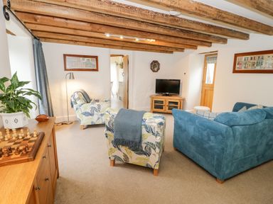 A living room with blue and patterned armchairs a television and wooden beams on the ceiling at The Old Stable in Henryd near Conwy
