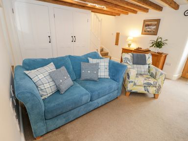 A living room with a blue sofa and a patterned armchair near a wooden cabinet with a lamp and a plant at The Old Stable in Henryd near Conwy