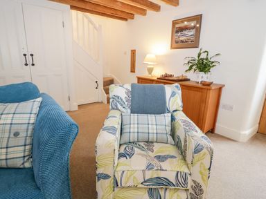 A sitting room with a patterned armchair blue sofa wooden cabinet and staircase at The Old Stable in Henryd near Conwy