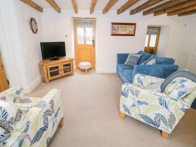 A living room with a blue sofa two patterned armchairs a wooden TV stand with a television and wooden beams on the ceiling at The Old Stable in Henryd near Conwy