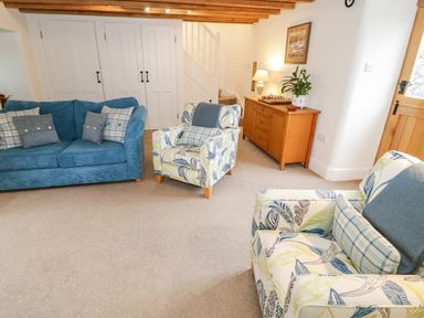 A living room with two patterned armchairs and a blue sofa near stairs and a wooden cabinet at The Old Stable in Henryd near Conwy