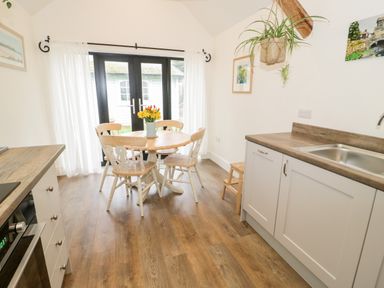 A kitchen with a wooden dining table and chairs a sink and countertop with cabinets and a hanging plant at The Old Stable in Henryd near Conwy