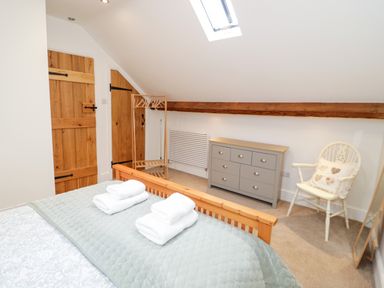 A bedroom with a wooden bed, folded towels, a gray dresser, a white chair with a cushion, wooden doors, and a skylight at The Old Stable in Henryd near Conwy