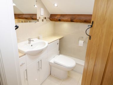 A small bathroom with a sink, toilet, counter, and wooden beam at The Old Stable in Henryd near Conwy
