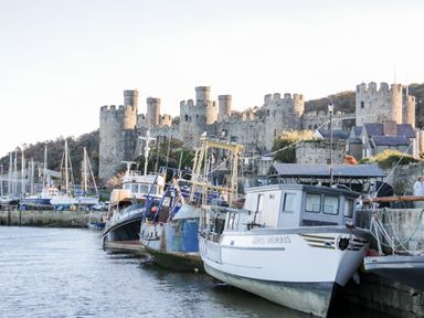 A harbor with boats docked and a stone castle in the background at Henryd near Conwy
