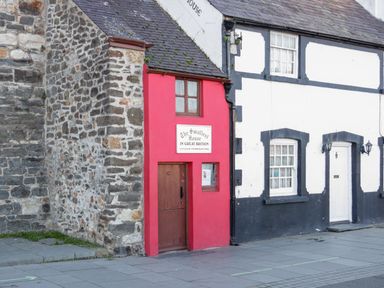 The smallest house in Great Britain with a red facade and brown door next to white and black painted buildings
