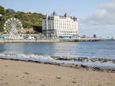 A beach with waves and a pier with a ferris wheel and a large hotel building at The Old Stable in Henryd near Conwy