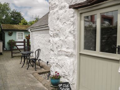 A small outdoor patio with a black metal table and two chairs next to a white stone wall and a door at The Old Stable in Henryd near Conwy