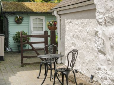 A small outdoor patio with a metal table and two chairs next to a white stucco wall and a green shed at The Old Stable in Henryd near Conwy