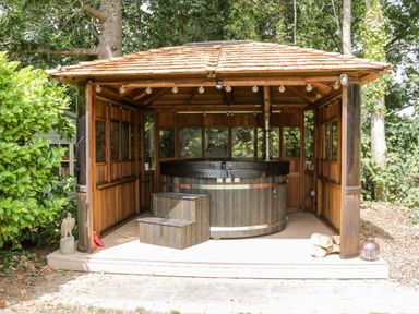An outdoor wooden gazebo with a hot tub and steps surrounded by trees at The Old Stable in Henryd near Conwy