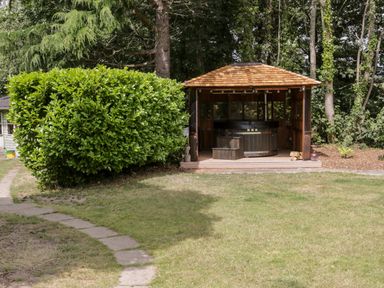 A garden with a path leading to a wooden hot tub gazebo and large bush at The Old Stable in Henryd near Conwy