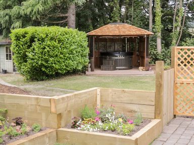A garden with a wooden gazebo housing a hot tub and a flower bed with a wooden fence at The Old Stable in Henryd near Conwy