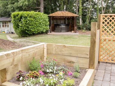 A garden with a wooden raised flower bed a wooden gazebo with a hot tub and a small shed in the background at The Old Stable in Henryd near Conwy