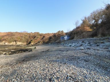 A rocky beach with small blue and white huts near bushes at The Headland in Llaneilian near Amlwch