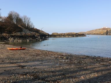 A rocky beach with a kayak and birds on the water at The Headland in Llaneilian near Amlwch