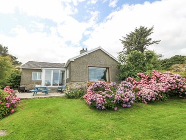 A garden with green grass and pink and purple flowers outside a house at The Headland in Llaneilian near Amlwch