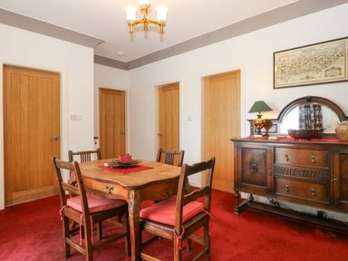 A dining room with a wooden table and four chairs on red carpet and a wooden sideboard with lamp and mirror at The Headland in Llaneilian near Amlwch