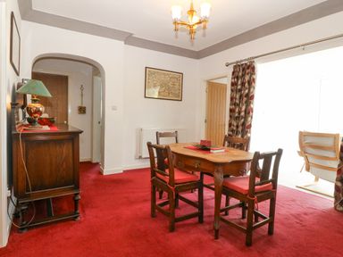 A dining room with wooden table and four chairs on red carpet at The Headland in Llaneilian near Amlwch
