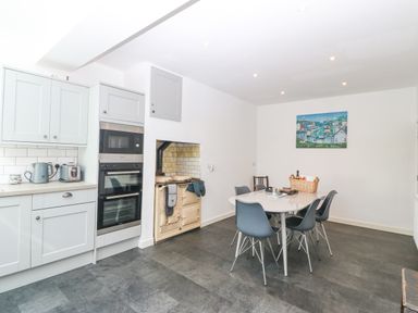 A kitchen with grey cabinets a stove and a dining table with chairs and a basket at The Headland in Llaneilian near Amlwch