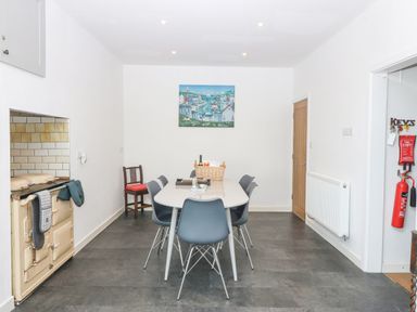 A dining room with a white table surrounded by blue chairs an old stove on the left and fire safety equipment on the right at The Headland in Llaneilian near Amlwch
