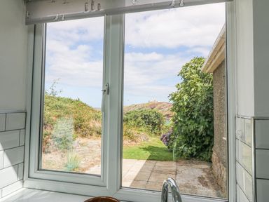 A view through a kitchen window showing a garden with a tiled patio and greenery at The Headland in Llaneilian near Amlwch