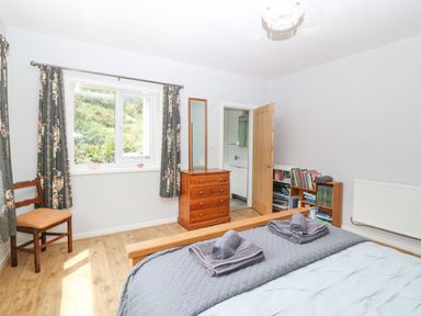 A bedroom with a bed folded towels wooden chest of drawers bookshelf chair and window at The Headland in Llaneilian near Amlwch