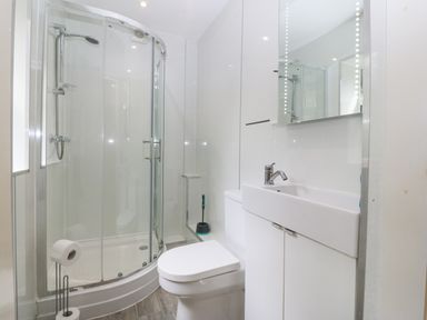 A bathroom with a curved glass shower enclosure a toilet a sink with a cabinet and a mirror at The Headland in Llaneilian near Amlwch