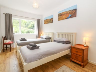 A bedroom with two single beds side by side with gray bedding and folded towels a wooden nightstand with a lamp two landscape paintings on the wall and a wooden chair by the window at The Headland in Llaneilian near Amlwch