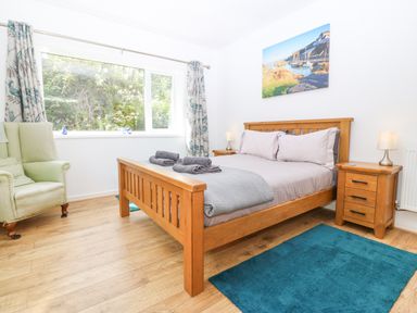 A bedroom with a wooden bed gray bedding two bedside tables with lamps a green armchair and a large window at The Headland in Llaneilian near Amlwch