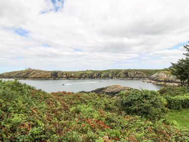 A coastline with rocky cliffs green bushes and a boat on the water at The Headland in Llaneilian near Amlwch