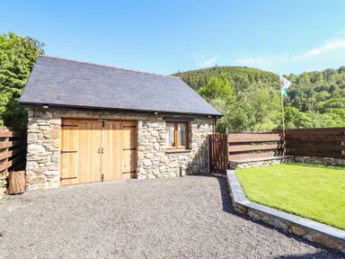 An exterior view of a stone building with wooden double doors next to a small grassy yard and wooden fencing at Glyndwr in Betws-Y-Coed